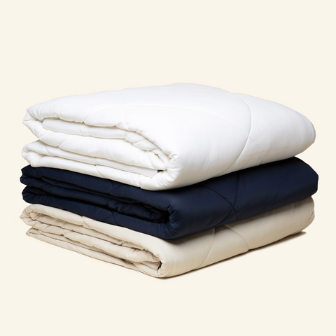 The Lightweight UltraCool Comforter folded and stacked in the Sand, white, and navy color