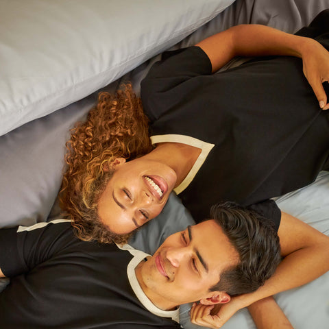 A young couple lying on a bed made with Slumber Cloud products.